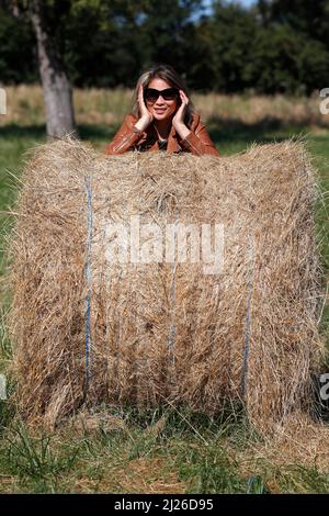 Frau mit einer Rolle Stroh in einem frisch geschnittenen Weizenfeld verpackt. Stockfoto