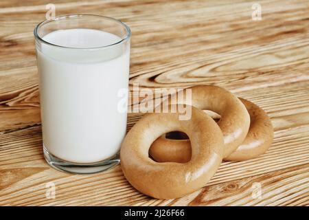 Ein Glas frische Milch und drei Bagels auf einem Holztisch. Stockfoto