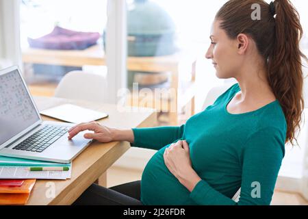 Online-Tipps für Erstmtter. Aufnahme einer Schwangeren, die ihren Laptop zu Hause benutzt. Stockfoto