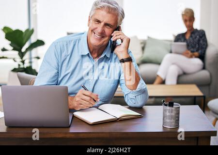Sie brauchen keine Büroräume, um ein erfolgreiches Unternehmen zu führen. Aufnahme eines reifen Mannes, der sich Notizen machte, während er auf seinem Handy sprach. Stockfoto