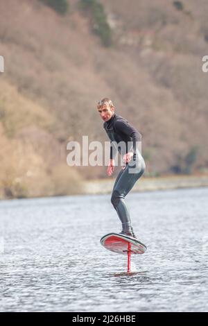 Nahaufnahme eines Surfers in einem auf einem walisischen See isolierten Neoprenanzug (Llyn Padarn), Wassersportarten, Ausgleich im Wasser auf einem Tragflächenboot. Stockfoto