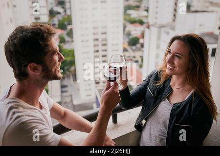Wir feiern unser Abenteuer durch die Stadt. Eine kleine Aufnahme eines attraktiven jungen Paares, das auf einem Dach mit Blick auf die Stadt Wein trinkt. Stockfoto