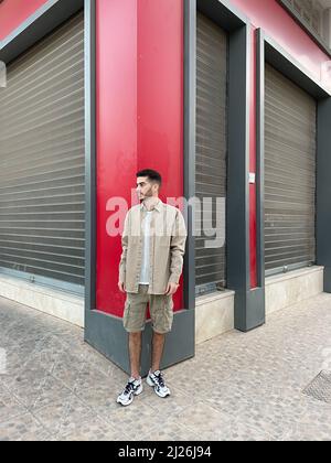 Attraktives Modell für junge Männer in grauer Weste und grauer, kurz stehender Garage gegenüber. Stockfoto