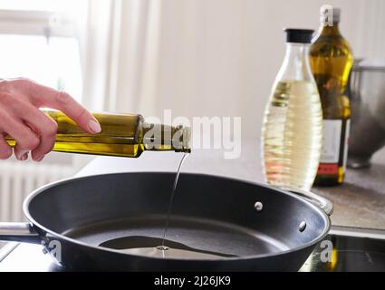 Berlin, Deutschland. 30. März 2022. ILUUSTRATION - Eine Frau gießt Sonnenblumenöl in eine Pfanne. Quelle: Annette Riedl/dpa/Alamy Live News Stockfoto