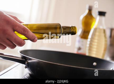 Berlin, Deutschland. 30. März 2022. ILUUSTRATION - Ein Mann gießt Sonnenblumenöl in eine Pfanne. Quelle: Annette Riedl/dpa/Alamy Live News Stockfoto