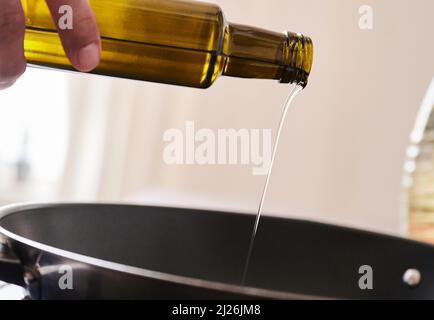 Berlin, Deutschland. 30. März 2022. ILUUSTRATION - Ein Mann gießt Sonnenblumenöl in eine Pfanne. Quelle: Annette Riedl/dpa/Alamy Live News Stockfoto