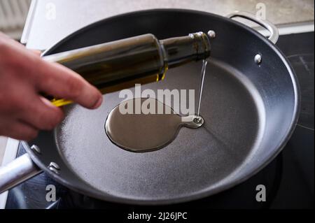 Berlin, Deutschland. 30. März 2022. ILUUSTRATION - Ein Mann gießt Sonnenblumenöl in eine Pfanne. Quelle: Annette Riedl/dpa/Alamy Live News Stockfoto