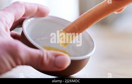 Berlin, Deutschland. 30. März 2022. ILLUSTRATION - Eine Frau taucht eine Wurst in den Senf. Quelle: Annette Riedl/dpa/Alamy Live News Stockfoto