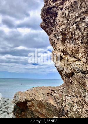 Nahaufnahme des Randes einer zerklüfteten Klippe an der Küste mit rauem, zerklüfteten Felsformationen im Hintergrund und trüben, dramatischen, himmelgrauen Wolken Stockfoto