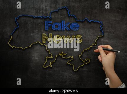 Das Mädchen schreibt auf der Tafel den Text Fake News auf der Karte der Ukraine Stockfoto
