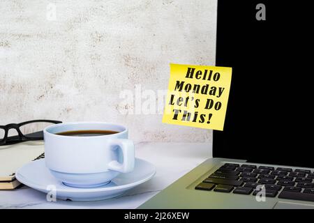 Inspirierende Zitate - Hallo Montag, lassen Sie uns diesen Text auf einer Haftnotiz auf dem Computerbildschirm mit anderem Zubehör und Kaffee auf einem weißen Tisch machen. Stockfoto