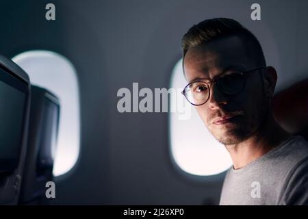 Porträt eines Mannes, der mit dem Flugzeug reist. Passagiere auf einem Fenstersitz mit Blick auf die Kamera. Stockfoto