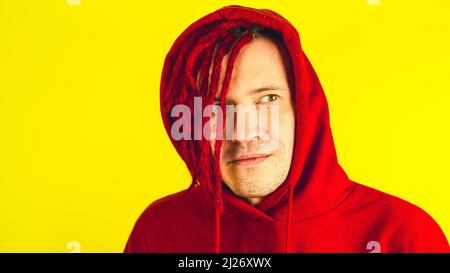 Junger Mann mit roten Dreadlocks in der Kapuze schaut weg. Portrait stilvoller Mann mit heller Frisur posiert im Studio Stockfoto