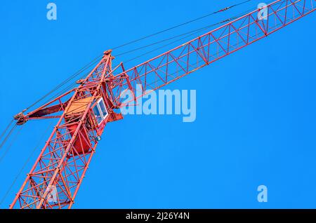 Baukran auf dem Hintergrund des blauen Himmels. Nahaufnahme der Kran-Fahrerkabine. Bauindustrie Stockfoto