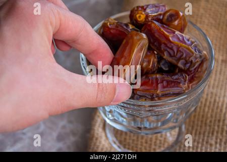Die Hand nimmt Datteln aus der Schüssel. Traditionelles iftar-Essen für muslime. Nahaufnahme. Stockfoto