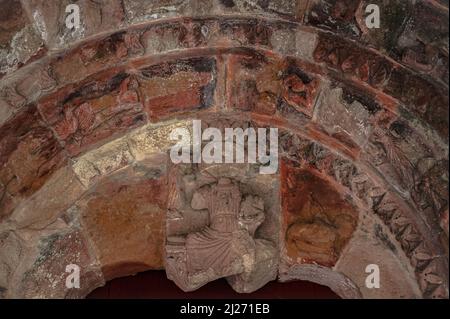 Ein kopfloser Christus in Majestät führt die verstümmelte und doch farbenfrohe romanische Skulptur aus dem Jahr 1100s n. Chr. auf dem Trommelfell über dem Nordeingang der ehemaligen Benediktinerkirche Saint-Jean de Sordes in Sorde l'Abbaye, Landes, Nouvelle-Aquitaine, Frankreich. Stockfoto