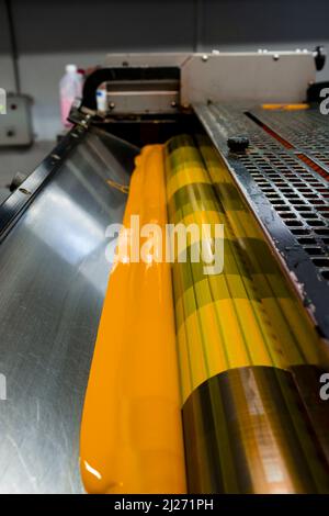 Farbe und glänzende Walzen von Offset-Druckmaschine. Offset-Farbe. Gelb. Vertikal aufgenommene Fotos, Vorderseite des Fotos mit ausgewähltem Fokus. Stockfoto