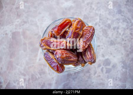 Getrocknete Datgelfrüchte in einer Schüssel auf Marmorboden. Draufsicht auf reife Datteln. Traditionelles iftar-Essen für muslime. Stockfoto