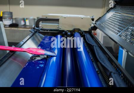 Farbe und glänzende Walzen von Offset-Druckmaschine. Offset-Farbe. Cyan. Horizontal aufgenommene Aufnahme, ausgewählter Fokuszylinder in der Mitte. Stockfoto