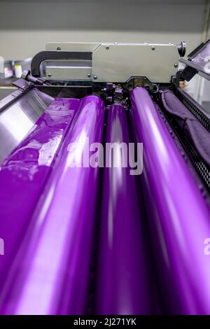 Farbe und glänzende Walzen von Offset-Druckmaschine. Offset-Farbe. Spot Purple. Vertikal aufgenommene Aufnahme, ausgewählter Fokuszylinder in der Mitte. Stockfoto