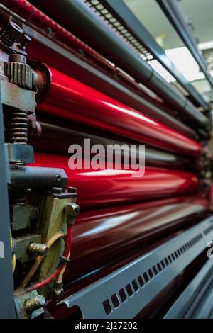 Farbe und glänzende Walzen von Offset-Druckmaschine. Offset-Farbe. Magenta. Horizontal aufgenommene Fotos, ausgewählter Fokus vorne links. Stockfoto