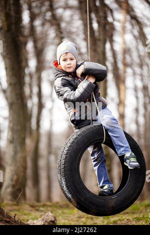 Glückliches Kind schwingt auf einem Autoreifen, der als Schaukel verwendet wurde. Stockfoto