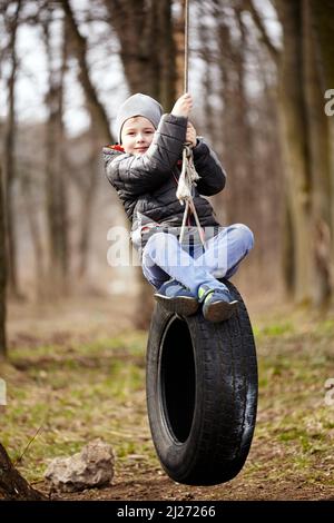 Glückliches Kind schwingt auf einem Autoreifen, der als Schaukel verwendet wurde. Stockfoto