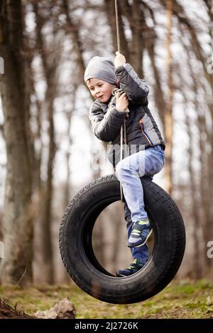 Glückliches Kind schwingt auf einem Autoreifen, der als Schaukel verwendet wurde. Stockfoto