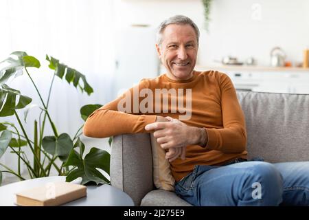 Lächelnder reifer Mann, der auf der Couch sitzt und posiert Stockfoto
