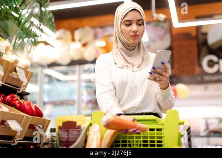Muslimische Junge Frau Beim Einkaufen Mit Dem Mobiltelefon Im Lebensmittelgeschäft Stockfoto