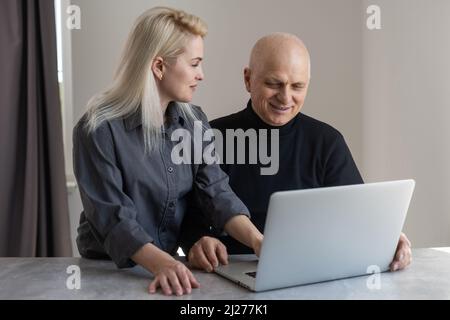 Attraktive junge Frau, die einem älteren Mann bei der Befragung hilft, Rentnerin, die Papiere im Pflegeheim ausfüllt, Hilfe hat Stockfoto
