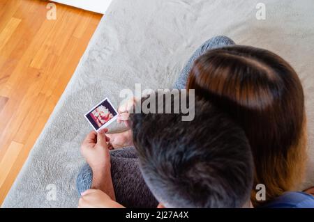Overhead-Ansicht schwanger heterosexuell junges Paar im Schlafzimmer sitzen auf dem Bett halten und Blick auf Ultraschall-Ausdruck Stockfoto