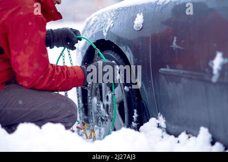 Junger Mann mit Handschuhen montieren Schneeketten im Auto Reifen im Winter auf Schnee Stockfoto