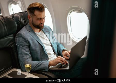 Bärtiger Mann, der im Flugzeug am Notebook arbeitet Stockfoto