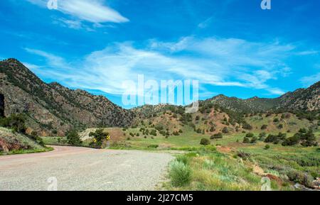 An einem warmen, schönen Tag schlängelt sich eine Straße um die Berge von Colorado. Blauer Himmel und weiße Wolken über den grünen Berggipfeln sind eine friedliche Umgebung. Stockfoto