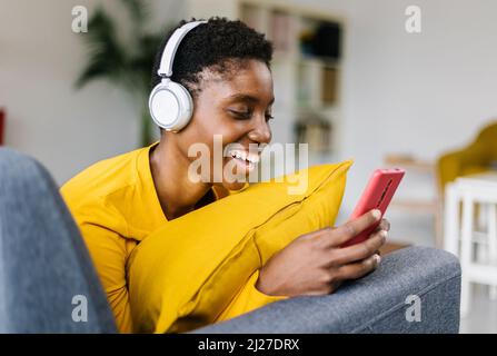 Multirassische afrikanerin, die mit Kopfhörern Musik hört, während sie das Mobiltelefon benutzt Stockfoto