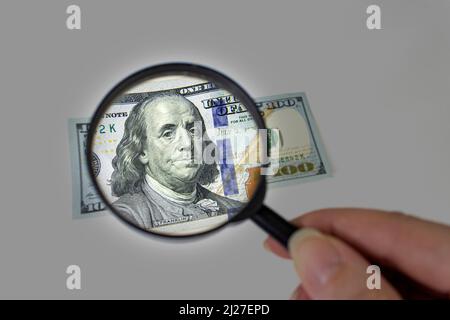 Hundert Dollar durch eine Lupe aus der Nähe. Untersuchung von gefälschtem Geld Stockfoto