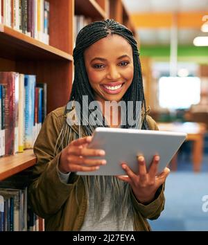 Es ist, als ob ich Hunderte von Büchern in meinen Händen halte. Porträt eines Studenten mit einem digitalen Tablet in der Bibliothek auf dem Campus. Stockfoto