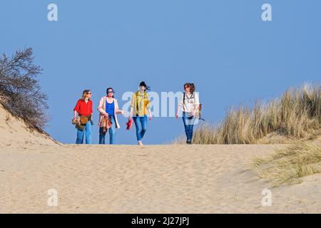 Vier glückliche Freundinnen mittleren Alters / Frauen in ihren 30s Jahren, die an einem sonnigen Frühlingstag in Sanddünen entlang der Nordseeküste wandern Stockfoto