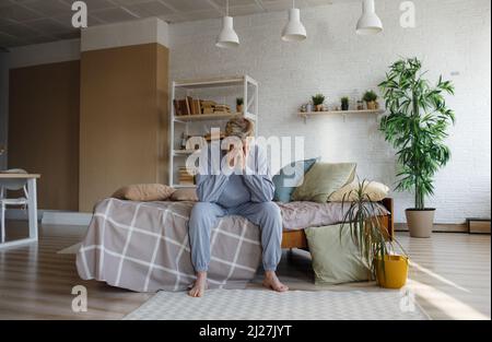 Porträt eines traurigen, nachdenklichen Mannes, der zu Hause auf einem Bett sitzt, seinen Kopf auf die Hände lehnt, an saisonalen Depressionen oder Lebensprobleme leidet, Feelin Stockfoto