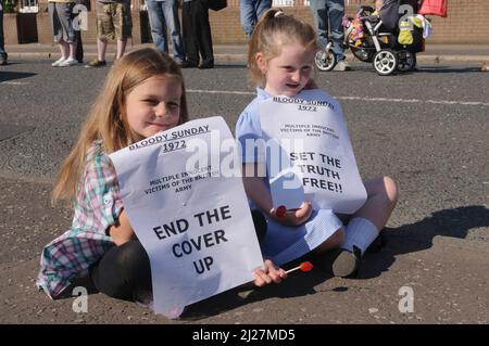 14/06/2010, Short Strand, Belfast, Nordirland. Kinder halten Protestplakate vor einem Protest mit schwarzer Flagge vor dem Saville Report on Bloody Sunday hoch Stockfoto