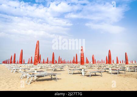 Rote Sonnenschirme und Sonnenliegen am Strand von Rimini - Italienischer Sommerüberblick zu Beginn der Saison Stockfoto