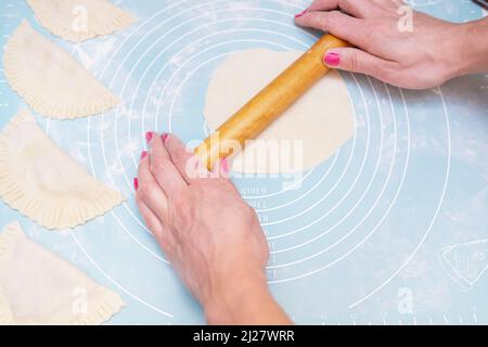 Testvorbereitung. Weibliche Hände Rollen den Teig mit einem Nudelholz auf einer Silikonmatte aus Stockfoto