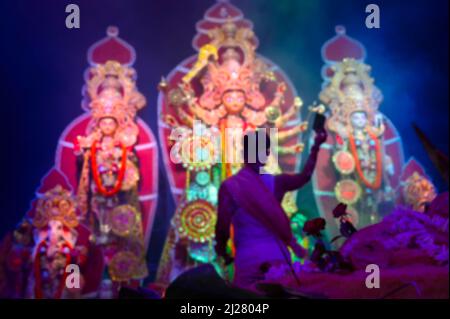 Das verschwommene Bild der Göttin Durga wird von einem hinduistischen Priester mit Spiegel verehrt. VOG, die heilige Speise wird Durga angeboten. Größtes Festival von Hind Stockfoto