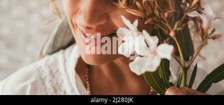 Nahaufnahme der Frau lächeln mit weißen Blumen im Vordergrund. Bannerbild von weiblichen Menschen, die glücklich lächeln. Heitere und fröhliche ausgewogene Lebensstil Menschen. Fotolia Stockfoto