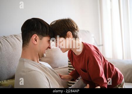Vater und Sohn schauen sich an und lächeln, während sie zu Hause Zeit miteinander genießen. Stockfoto