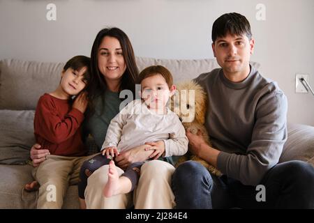 Porträt einer glücklichen Familie, die mit ihrem Hund zu Hause auf dem Sofa sitzt. Stockfoto