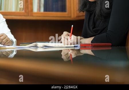 Die Rechtsanwältin schreibt in ihrem Notizbuch in einem kleinen Konferenzraum auf einem Reflex-Glastisch im asiatischen Stil einen Punkt für die Besprechungminute. Stockfoto