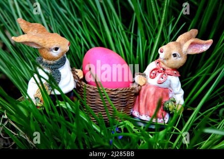 Frohe Osterpostkarte oder Poster mit zwei Kaninchen, die rotes Osterei auf grünem Grasgrund tragen Stockfoto