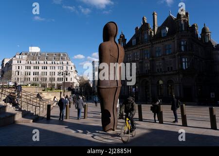 Menschen interagieren mit der Iron:man-Statue des britischen Bildhauers Antony Gormley am 14.. März 2022 auf dem Victoria Square in Birmingham, Großbritannien. Die Statue ist 6 Meter hoch, einschließlich der Füße, die unter dem Bürgersteig begraben sind, und wiegt 6 Tonnen. Die Statue lehnt sich um 7,5 Grad nach hinten und um 5 Grad nach links. Es wird vom Bildhauer gesagt, die traditionellen Fähigkeiten von Birmingham und dem Schwarzen Land zu repräsentieren, die während der industriellen Revolution praktiziert wurden. Die Statue wurde im September 2017 gelagert, um die Gleise für die U-Bahn-Erweiterung der West Midlands zum Centenary Square zu legen, und Stockfoto